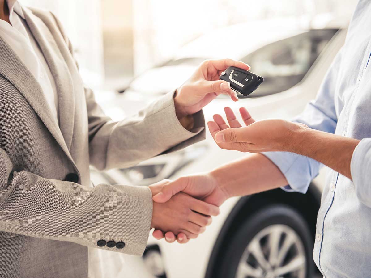 Une femme qui serre la main d'un homme en lui remettant les clés de sa voiture